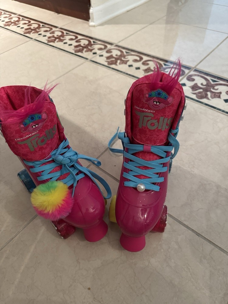 Vibrant Trolls-themed quad skates. Hot pink boot with blue laces. Rainbow pom-