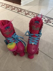 Vibrant Trolls-themed quad skates. Hot pink boot with blue laces. Rainbow pom-