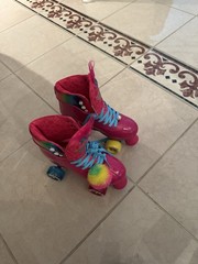 Vibrant Trolls-themed quad skates. Hot pink boot with blue laces. Rainbow pom-